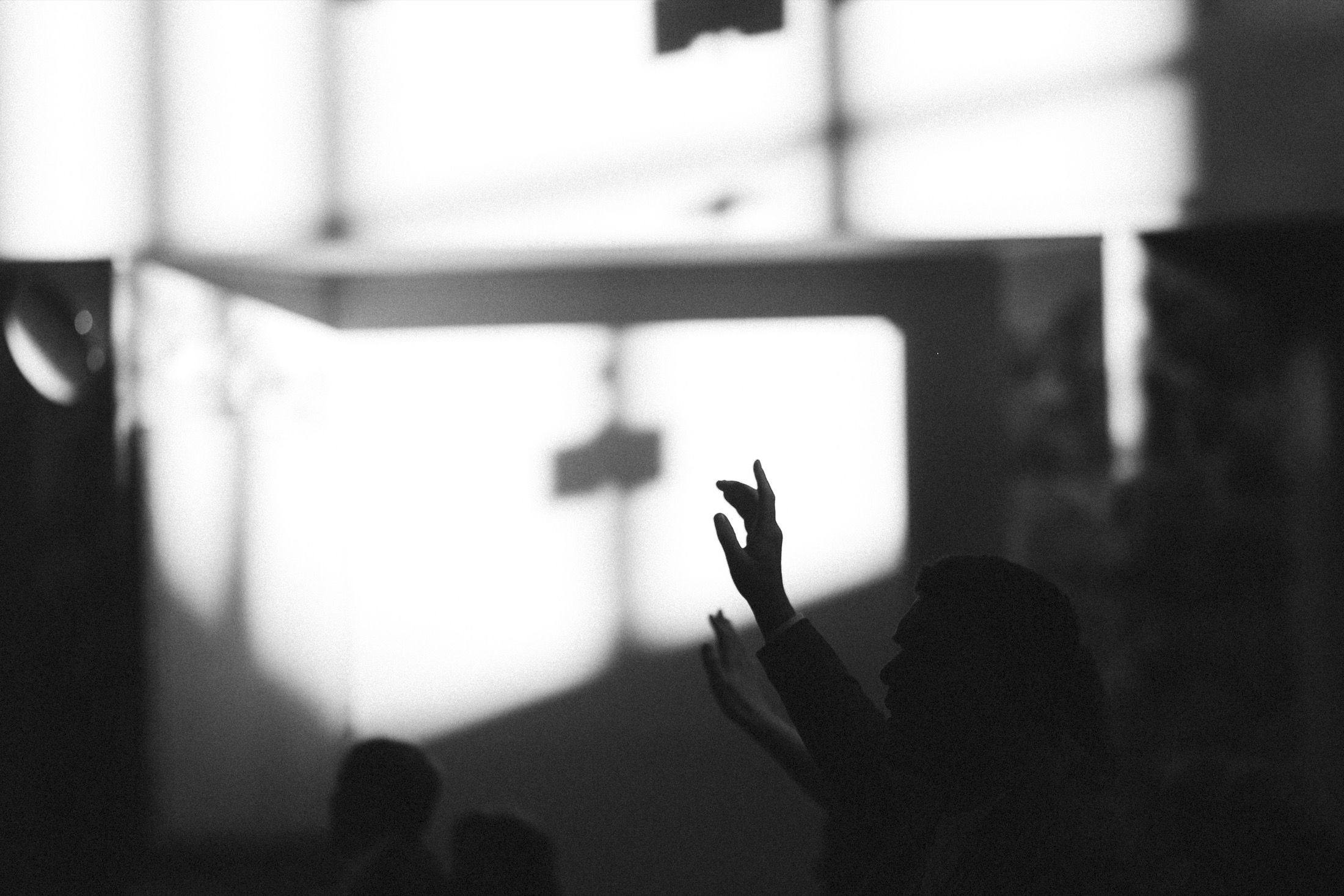 Silhouette of a hand raised in worship against window light